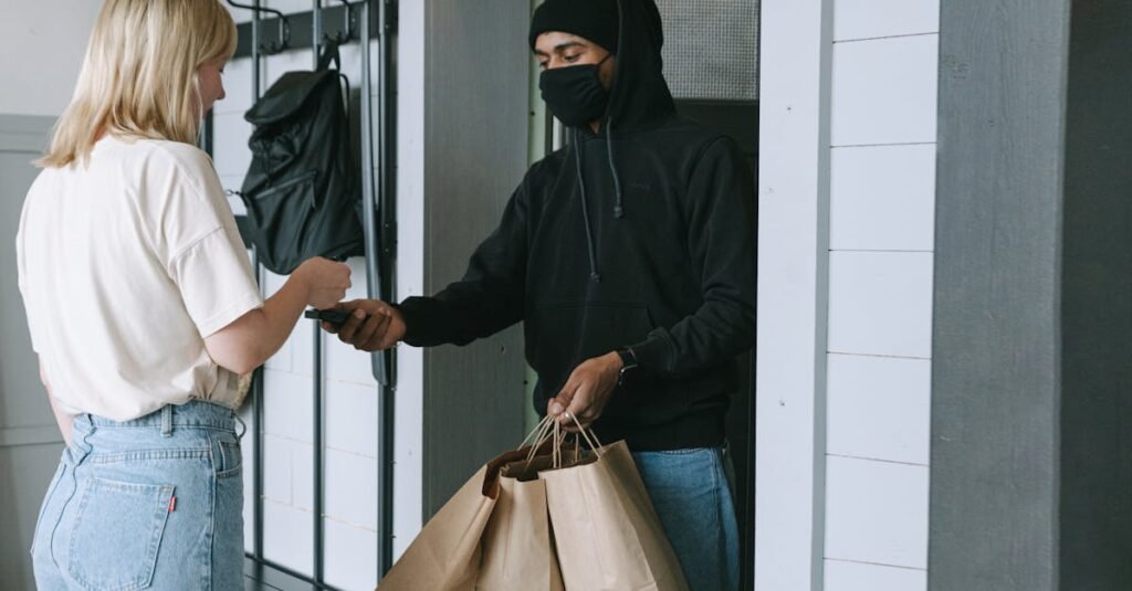 A delivery person hands over paper bags to a customer at the door in a contactless transaction.